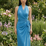 Two professional models wearing elegant halter-neck wrap maxi dresses in heather grey and vibrant sky blue, featuring a sophisticated draped V-neckline and waist tie for a minimalist summer or resort look.