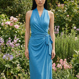 Two professional models wearing elegant halter-neck wrap maxi dresses in heather grey and vibrant sky blue, featuring a sophisticated draped V-neckline and waist tie for a minimalist summer or resort look.