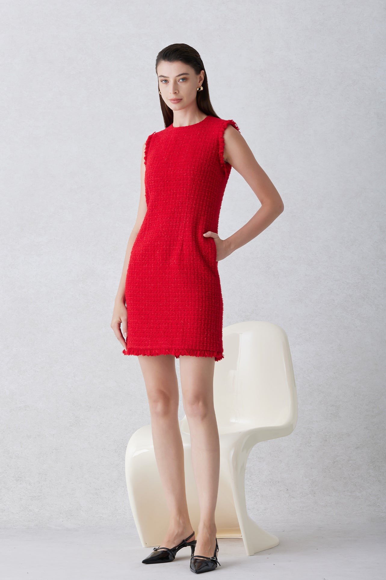 A professional woman wearing a sophisticated vibrant red tweed sleeveless mini dress, featuring a classic round neck, elegant frayed edges, and a slimming black waist belt for a chic holiday or office look.