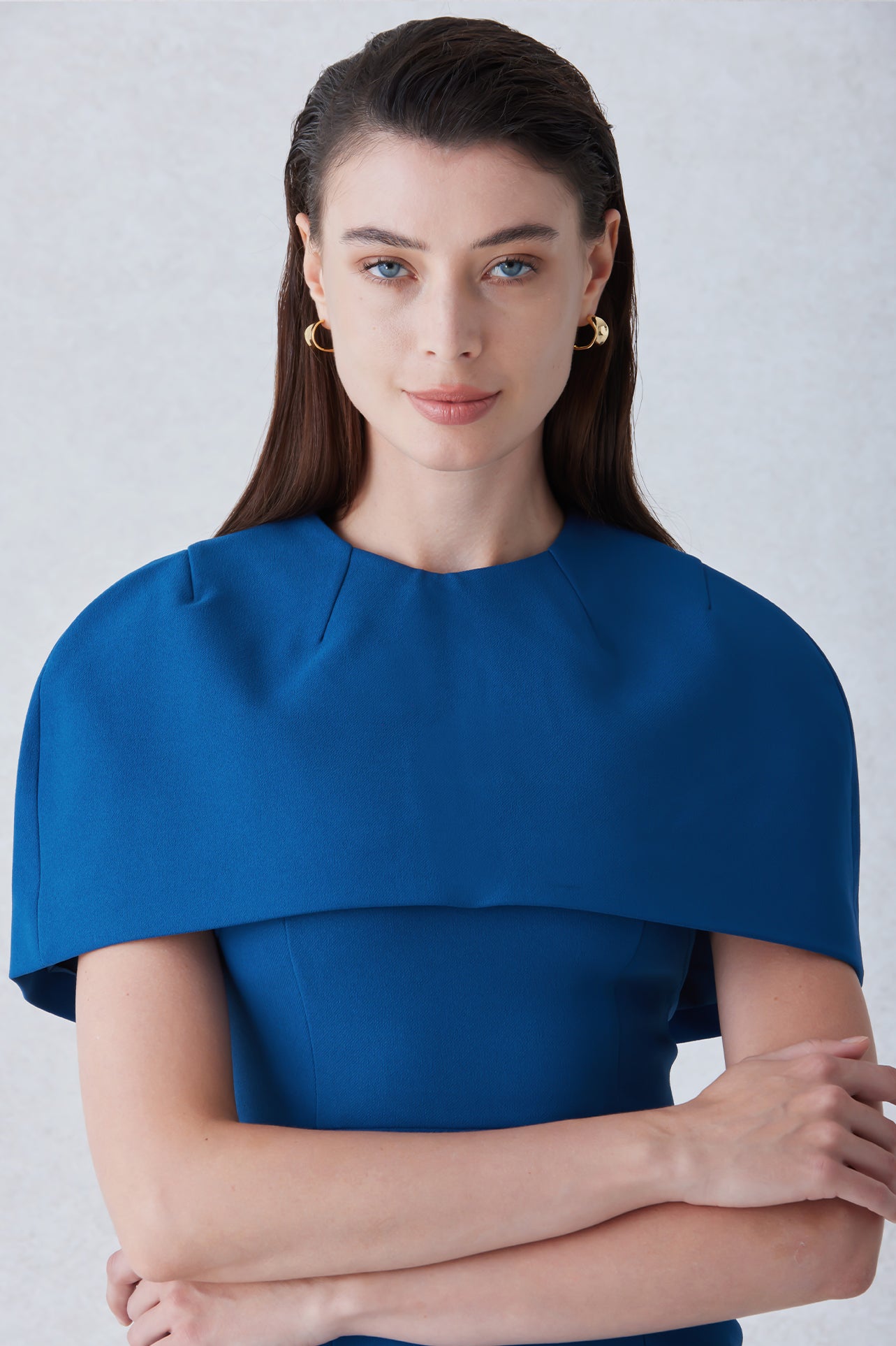 A professional woman wearing a sophisticated teal blue midi dress with an elegant cape-style overlay and structured shoulders, perfect for formal executive events and ceremonial occasions.