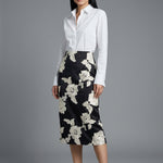 A professional woman wearing a classic crisp white long-sleeve slim-fit blouse with a sharp point collar, styled with a navy blue pencil skirt for a polished executive office look.