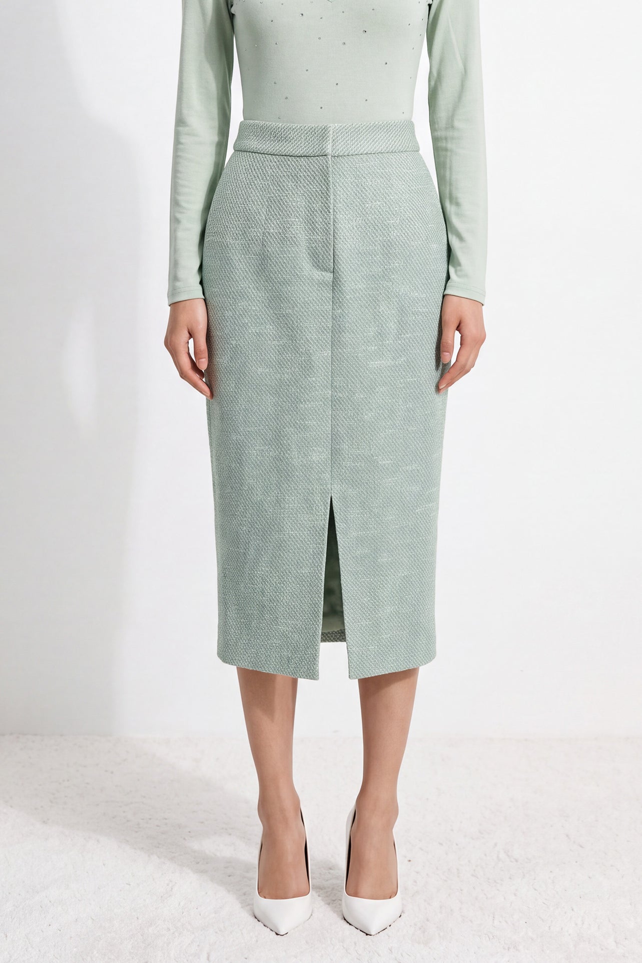 A woman wearing an elegant high-waisted mint green textured pencil midi skirt featuring a clean front waistband and a sophisticated front center slit for a refined corporate chic look.