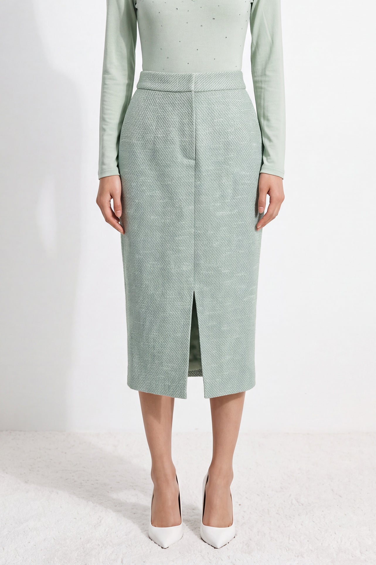 A woman wearing an elegant high-waisted mint green textured pencil midi skirt featuring a clean front waistband and a sophisticated front center slit for a refined corporate chic look.