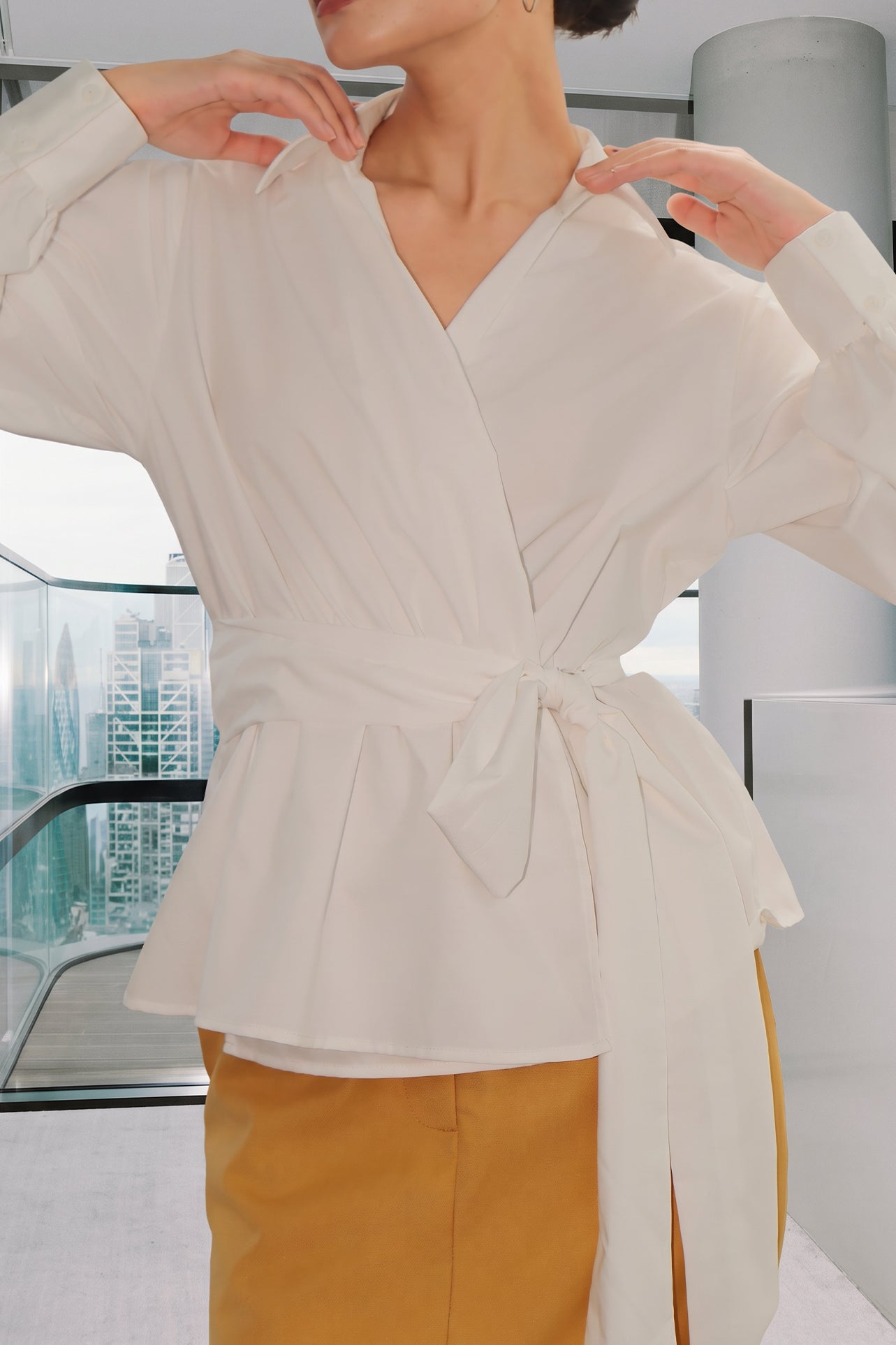 A stylish woman posing against a city skyline wearing a navy blue wrap blouse with golden ginkgo leaf print tied