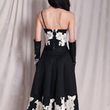 An elegant woman wearing a sophisticated black A-line midi dress, featuring exquisite white floral embroidery along the hem and professional three-quarter sleeves for a timeless formal look.