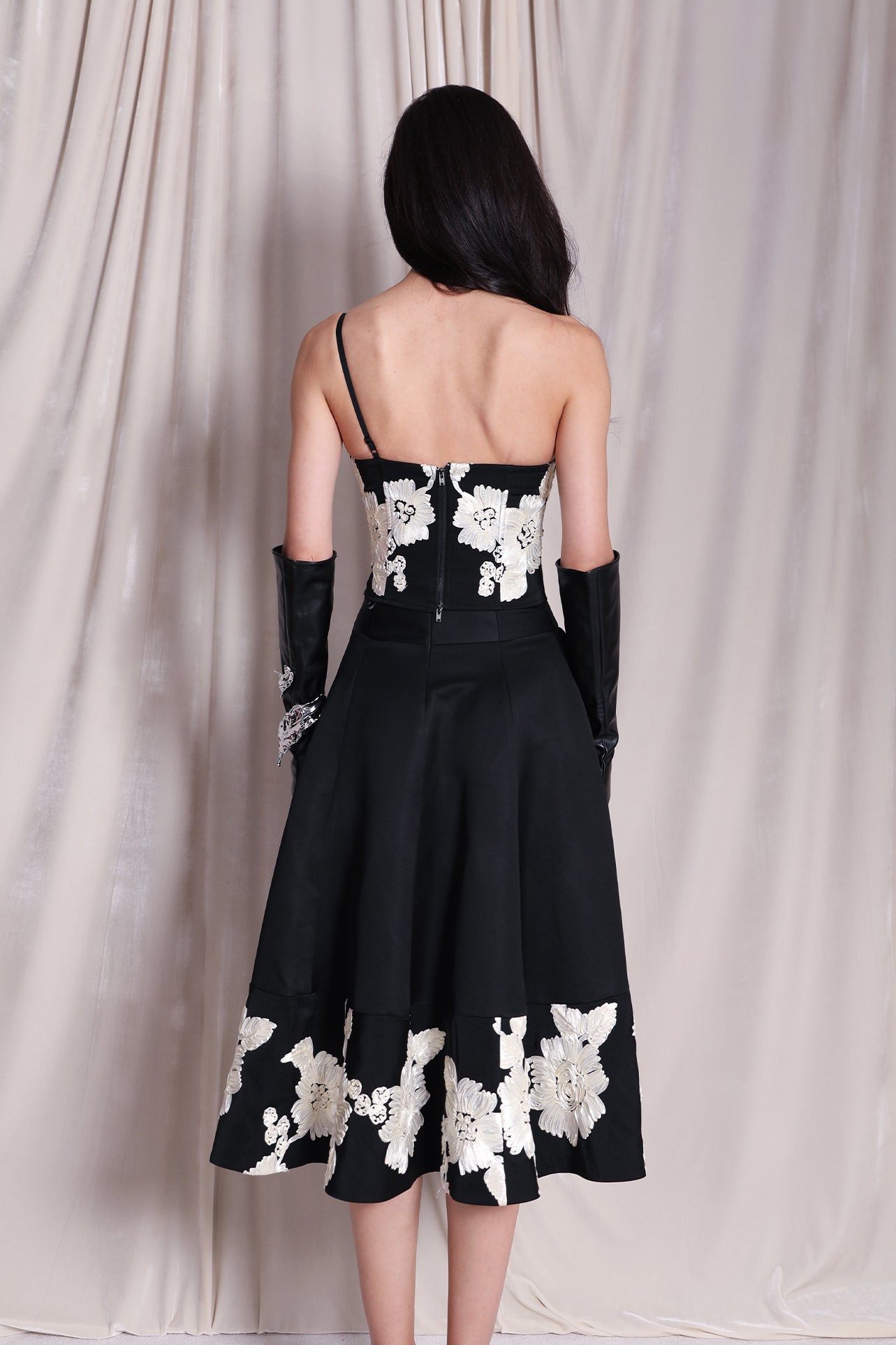 An elegant woman wearing a sophisticated black A-line midi dress, featuring exquisite white floral embroidery along the hem and professional three-quarter sleeves for a timeless formal look.