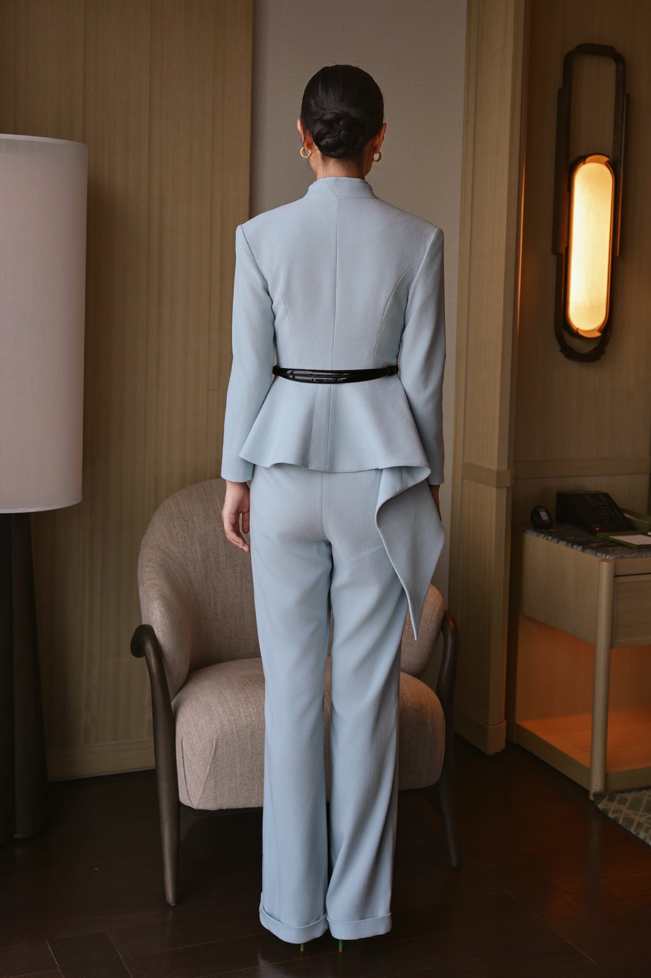 A style comparison of three women wearing tailored two-piece power suits featuring long-sleeve split V-neck jackets with dramatic asymmetrical peplum hems and matching cuffed wide-leg trousers; shown in vibrant crimson red, deep navy blue, and pale ice blue.