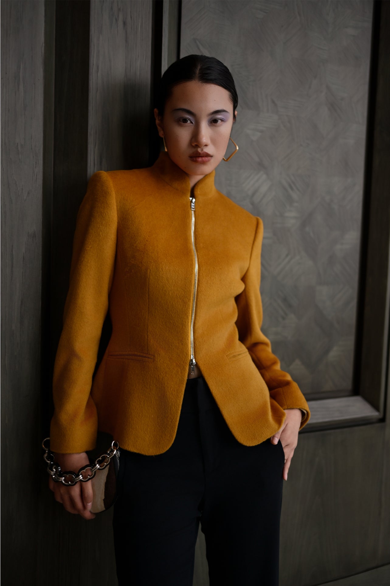 A chic professional Asian woman wearing a luxurious camel wool tailored jacket featuring a sleek stand collar, exposed two-way front zipper, structured shoulders, and an hourglass silhouette paired with a matching skirt.