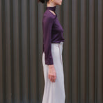 A chic woman wearing an elegant deep plum long-sleeve blouse with an asymmetric high-neck scarf tie, neatly tucked into a high-waisted black tweed skirt embellished with subtle sparkling sequins.