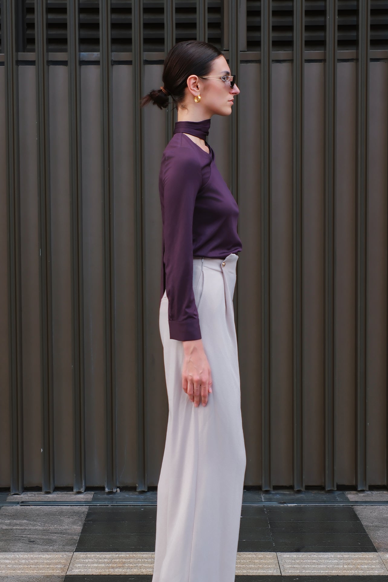 A chic woman wearing an elegant deep plum long-sleeve blouse with an asymmetric high-neck scarf tie, neatly tucked into a high-waisted black tweed skirt embellished with subtle sparkling sequins.