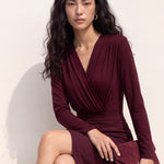 A style comparison of two elegant long-sleeve V-neck wrap tops featuring delicate shoulder pleating and a sleek tucked-in fit; the left in warm camel paired with cream trousers, and the right in deep burgundy paired with black trousers.