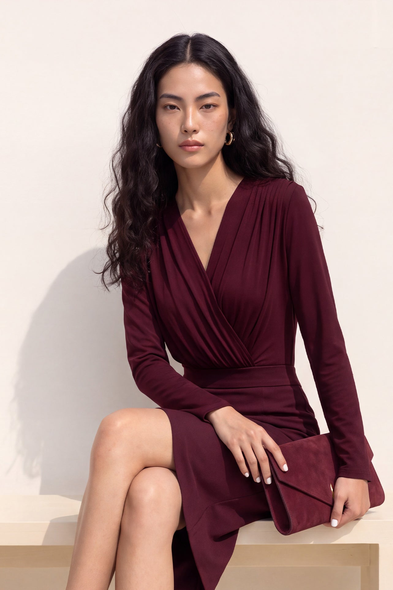 A style comparison of two elegant long-sleeve V-neck wrap tops featuring delicate shoulder pleating and a sleek tucked-in fit; the left in warm camel paired with cream trousers, and the right in deep burgundy paired with black trousers.