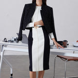 A professional woman wearing a sophisticated black and white color-block midi dress, featuring slimming side panels, long sleeves, and an elegant black belt with a gold buckle for a modern executive office look.
