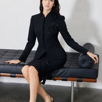 A professional woman wearing a sophisticated black skirt suit, featuring a mandarin collar with elegant leaf embroidery on the shoulder and skirt, and traditional frog button detailing for a modern oriental executive look.