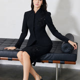 A professional woman wearing a sophisticated black skirt suit, featuring a mandarin collar with elegant leaf embroidery on the shoulder and skirt, and traditional frog button detailing for a modern oriental executive look.