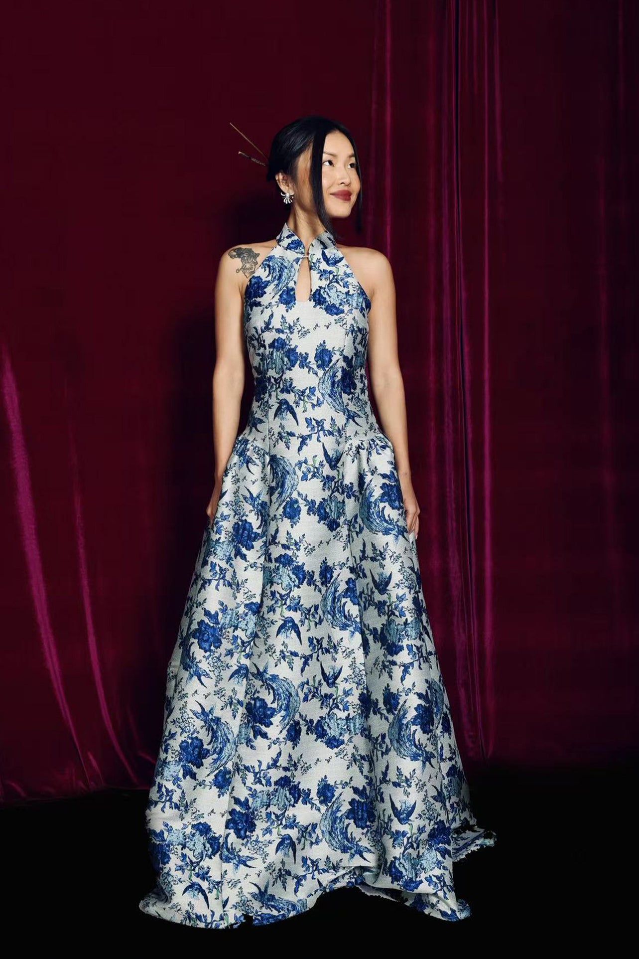 A stunning modern oriental gala dress featuring a classic blue and white porcelain floral print, an elegant halter neck with keyhole detail, and a voluminous A-line full skirt for a sophisticated formal look.