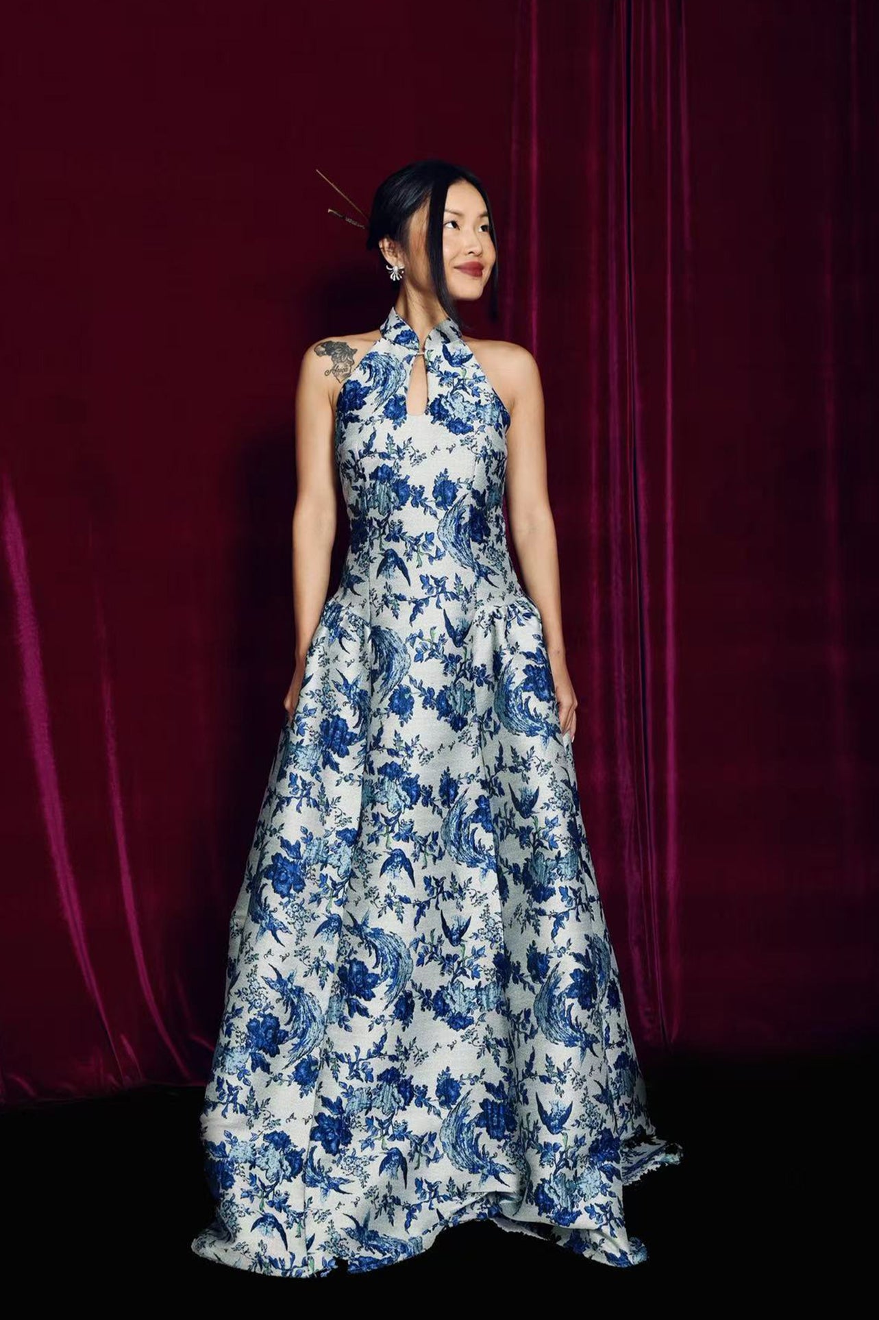 A stunning modern oriental gala dress featuring a classic blue and white porcelain floral print, an elegant halter neck with keyhole detail, and a voluminous A-line full skirt for a sophisticated formal look.