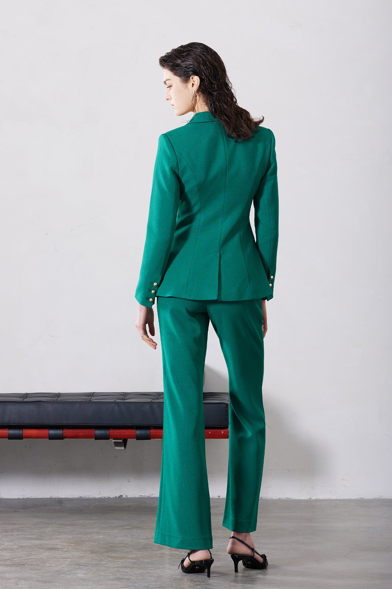 A professional woman wearing sophisticated emerald green high-waisted flare trousers, featuring a tailored slim fit through the hip and a stylish bootcut silhouette for an elegant office look.