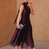 A chic woman wearing sunglasses and an elegant deep burgundy sleeveless V-neck A-line midi dress featuring textured jacquard fabric, delicate lace hemline, and a matching flowing neck scarf.