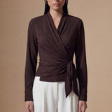 Two models presenting versatile textured wrap tops in cream and dark chocolate, featuring a slimming V-neck and elegant side-tie waist, styled with a tan pencil skirt and white high-waisted trousers.