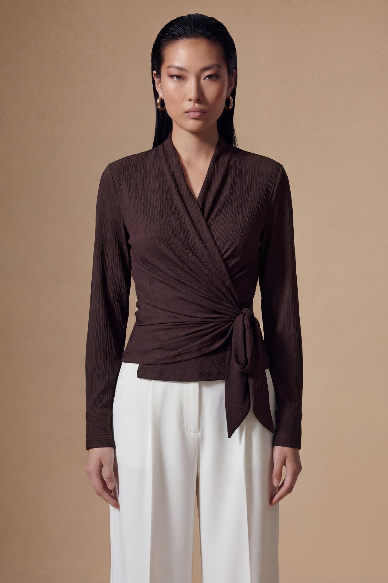 Two models presenting versatile textured wrap tops in cream and dark chocolate, featuring a slimming V-neck and elegant side-tie waist, styled with a tan pencil skirt and white high-waisted trousers.