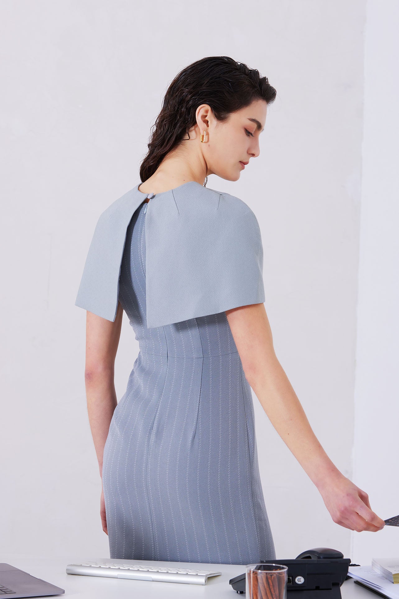 A professional woman wearing a sophisticated light grey pinstripe sleeveless sheath dress, featuring an elegant boat neckline and a tailored slim-fit silhouette for a polished executive look.