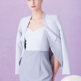 A professional woman wearing a sophisticated light grey tailored suit set, featuring a unique wrap-front blazer with criss-cross waist detailing and matching slim-fit trousers for a polished executive look.