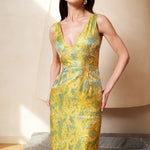A professional woman wearing a stunning gold and teal jacquard sheath dress, featuring a sophisticated V-neckline and elegant artistic wave patterns for a high-end formal look.
