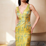 A professional woman wearing a stunning gold and teal jacquard sheath dress, featuring a sophisticated V-neckline and elegant artistic wave patterns for a high-end formal look.