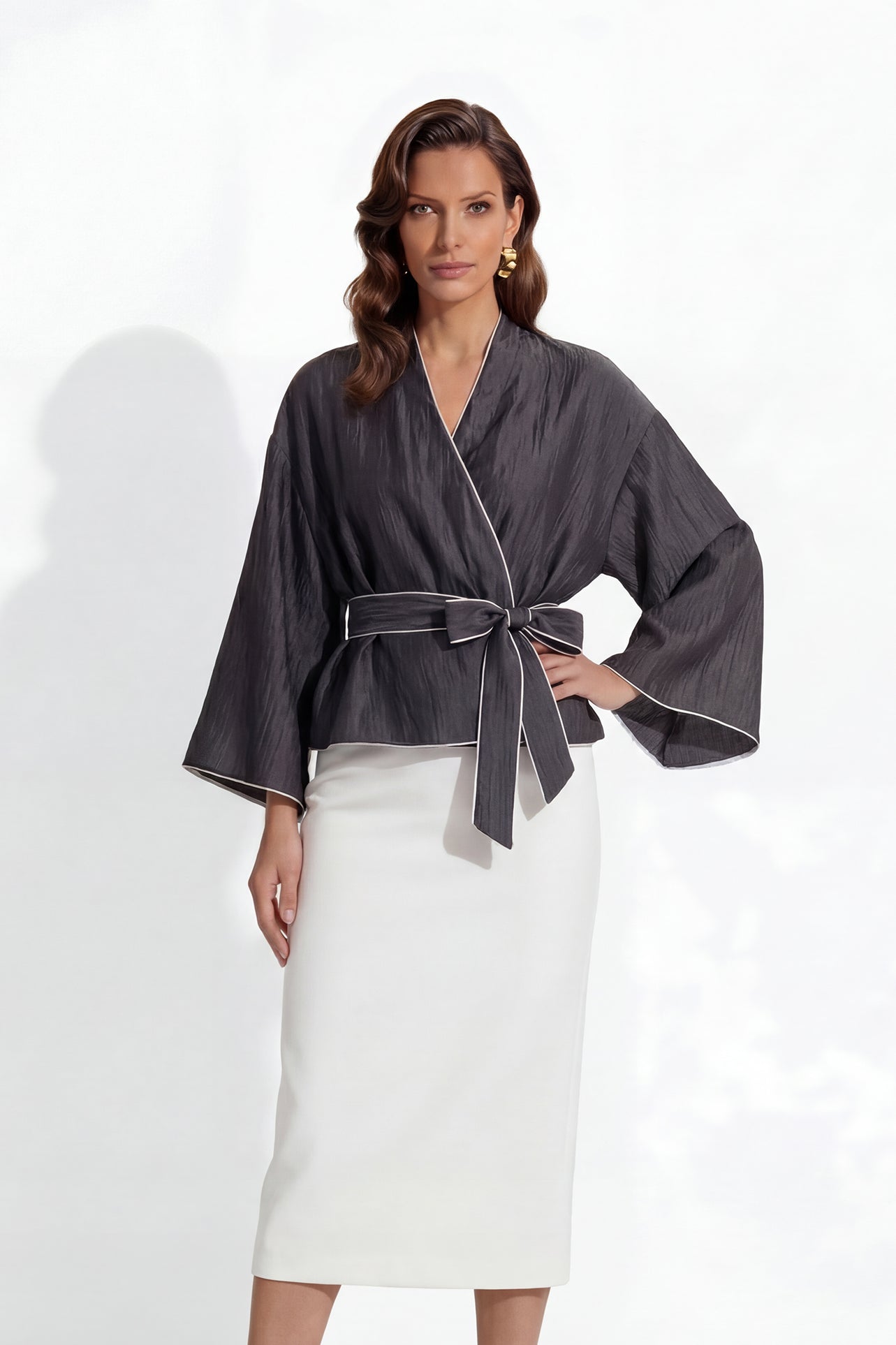 Two professional models wearing elegant shimmering satin wrap tops with kimono-style sleeves and waist ties, one in champagne gold and the other in charcoal grey with contrast white piping, paired with ivory high-waisted trousers.
