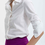 A professional woman wearing a classic crisp white long-sleeve slim-fit blouse with a sharp point collar, styled with a navy blue pencil skirt for a polished executive office look.