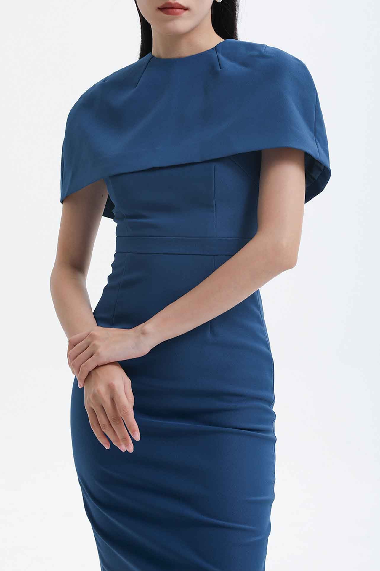 A professional woman wearing a sophisticated teal blue midi dress with an elegant cape-style overlay and structured shoulders, perfect for formal executive events and ceremonial occasions.