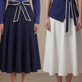 A comparison of two elegant professional looks: a navy blue pleated midi skirt and a crisp white flare skirt, both featuring sophisticated contrast-piped bow belts for a polished executive appearance.