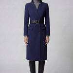 An elegant professional woman wearing a sophisticated navy blue double-breasted long coat dress, featuring a black waist belt and structured shoulders for a powerful executive look.