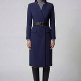 An elegant professional woman wearing a sophisticated navy blue double-breasted long coat dress, featuring a black waist belt and structured shoulders for a powerful executive look.