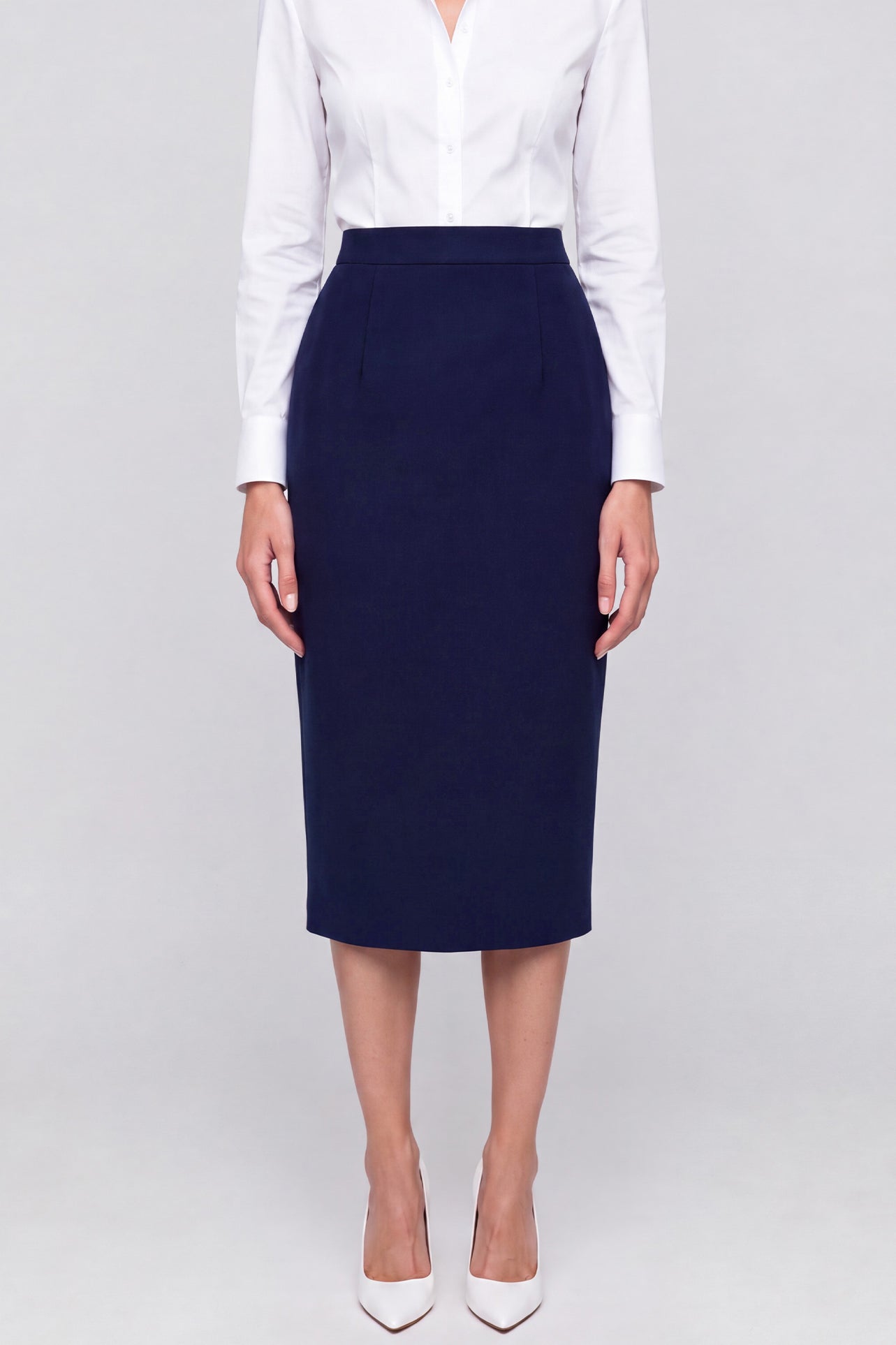 A professional woman wearing a classic navy blue high-waisted tailored pencil midi skirt with subtle front darts, neatly paired with a crisp white long-sleeve button-down shirt for an elegant corporate look.