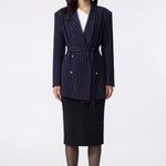 A professional woman wearing a sophisticated navy blue pinstripe blazer jacket, featuring a longline silhouette with a matching tie-waist belt and gold earring accents for an elegant executive office look.