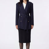 A professional woman wearing a sophisticated navy blue pinstripe blazer jacket, featuring a longline silhouette with a matching tie-waist belt and gold earring accents for an elegant executive office look.