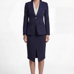 A professional woman wearing a sophisticated navy blue pinstripe suit, featuring a tailored single-button blazer and a matching midi pencil skirt with a front slit for an elegant executive office look.