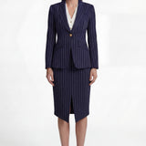 A professional woman wearing a sophisticated navy blue pinstripe suit, featuring a tailored single-button blazer and a matching midi pencil skirt with a front slit for an elegant executive office look.