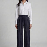 A professional woman wearing sophisticated navy blue pinstripe wide-leg trousers, featuring a high-waisted tailored fit and elegant vertical stripes for a polished executive office look.