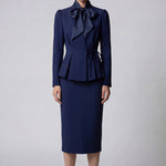 A professional woman wearing a sophisticated navy blue blazer, featuring an elegant pussy-bow neck tie, a flattering tie-waist wrap design, and subtle puff sleeves for a polished executive look.