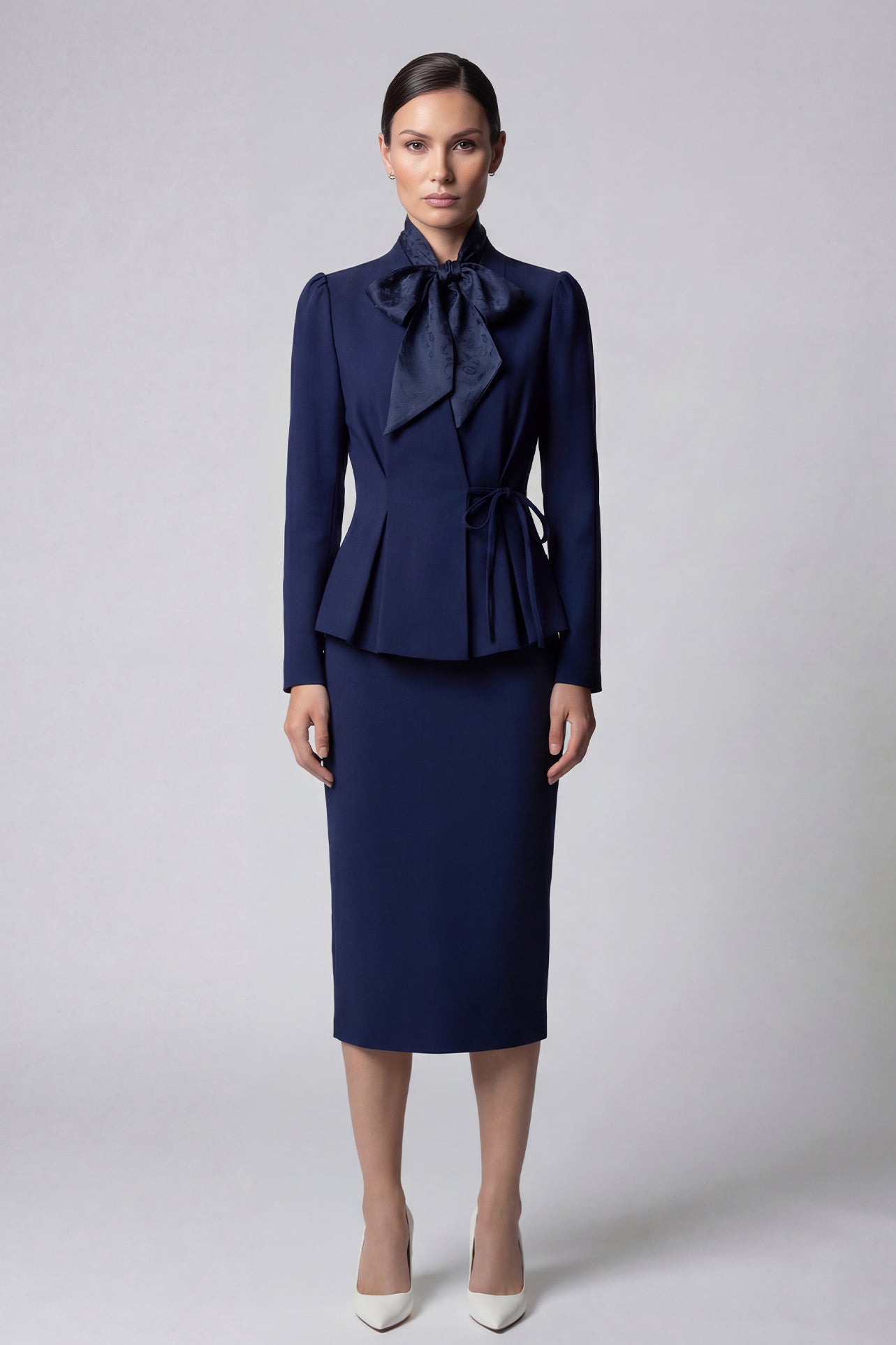 A professional woman wearing a sophisticated navy blue blazer, featuring an elegant pussy-bow neck tie, a flattering tie-waist wrap design, and subtle puff sleeves for a polished executive look.