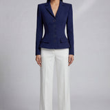 A professional model wearing a sophisticated navy blue tailored blazer with an hourglass silhouette and unique O-ring gold buttons, paired with crisp white trousers for an executive office look.