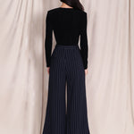 A professional woman wearing sophisticated navy blue pinstripe wide-leg trousers, featuring a high-waisted tailored fit and elegant vertical stripes for a polished executive office look.