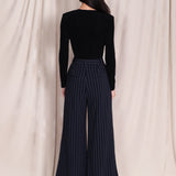 A professional woman wearing sophisticated navy blue pinstripe wide-leg trousers, featuring a high-waisted tailored fit and elegant vertical stripes for a polished executive office look.