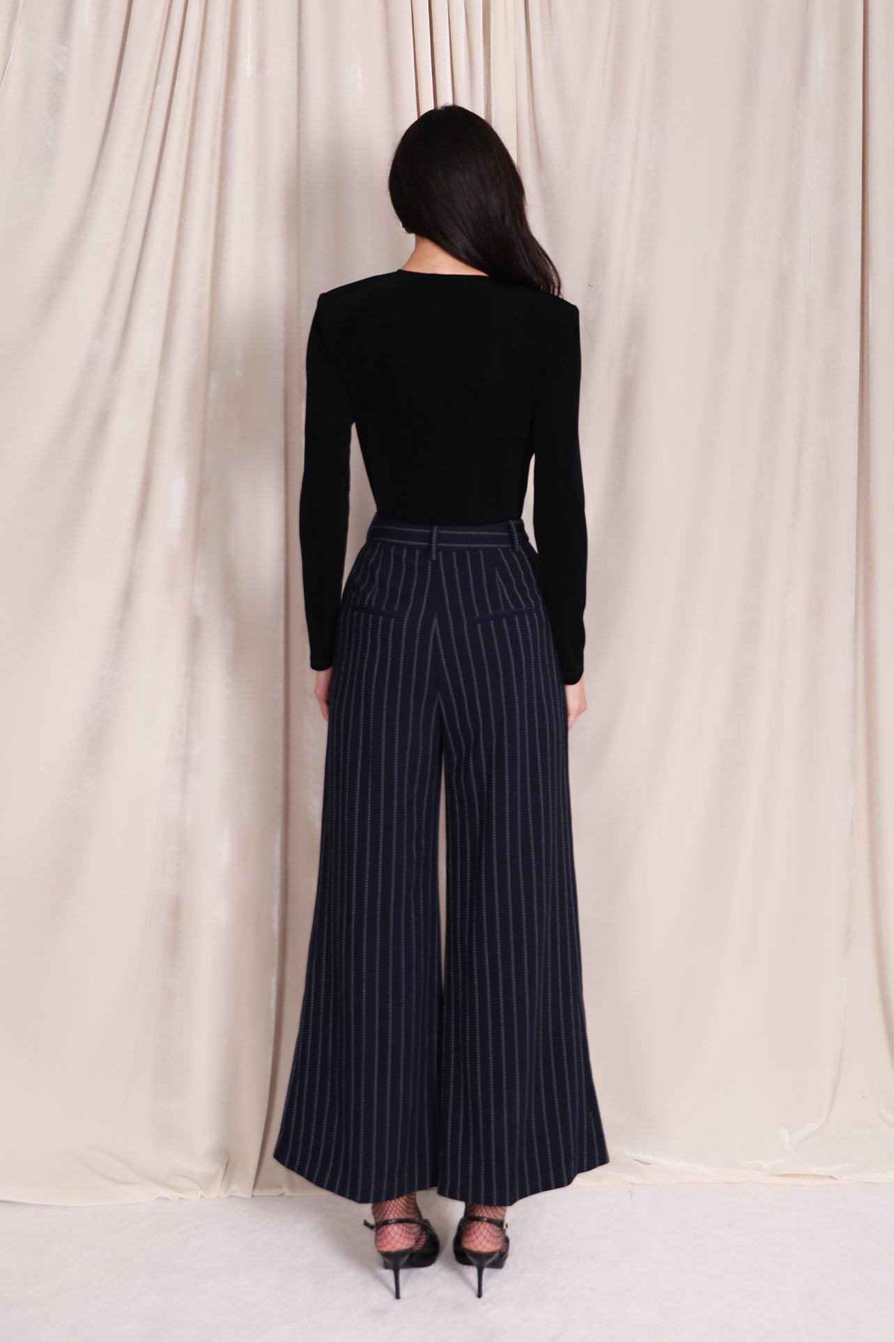 A professional woman wearing sophisticated navy blue pinstripe wide-leg trousers, featuring a high-waisted tailored fit and elegant vertical stripes for a polished executive office look.