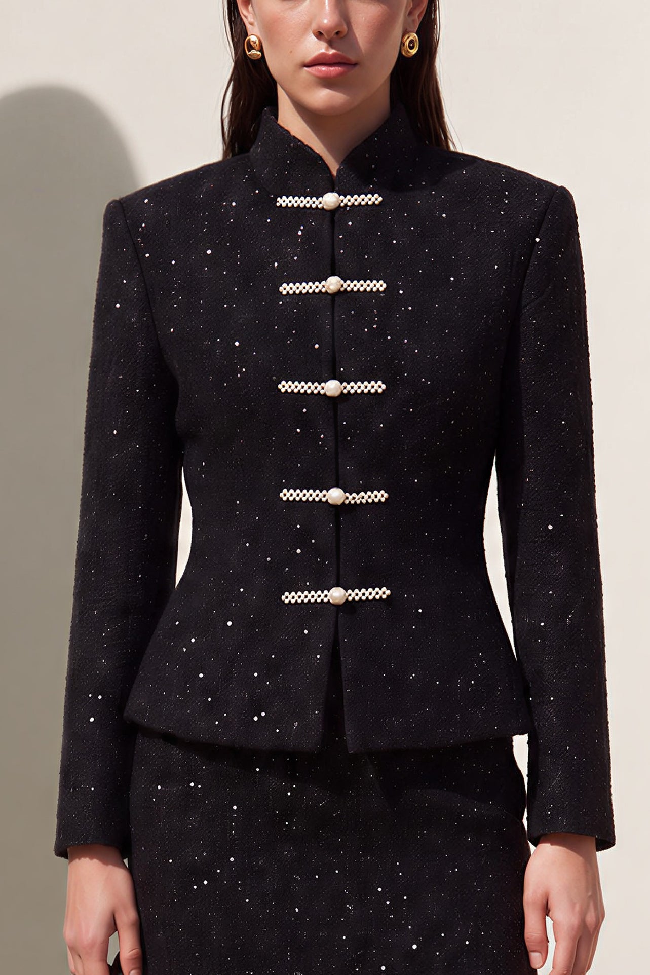 A chic woman wearing a luxurious black sparkle tweed tailored jacket featuring an authentic stand cheongsam collar, elegant horizontal pearl bar closures, and a flattering hourglass waistline.