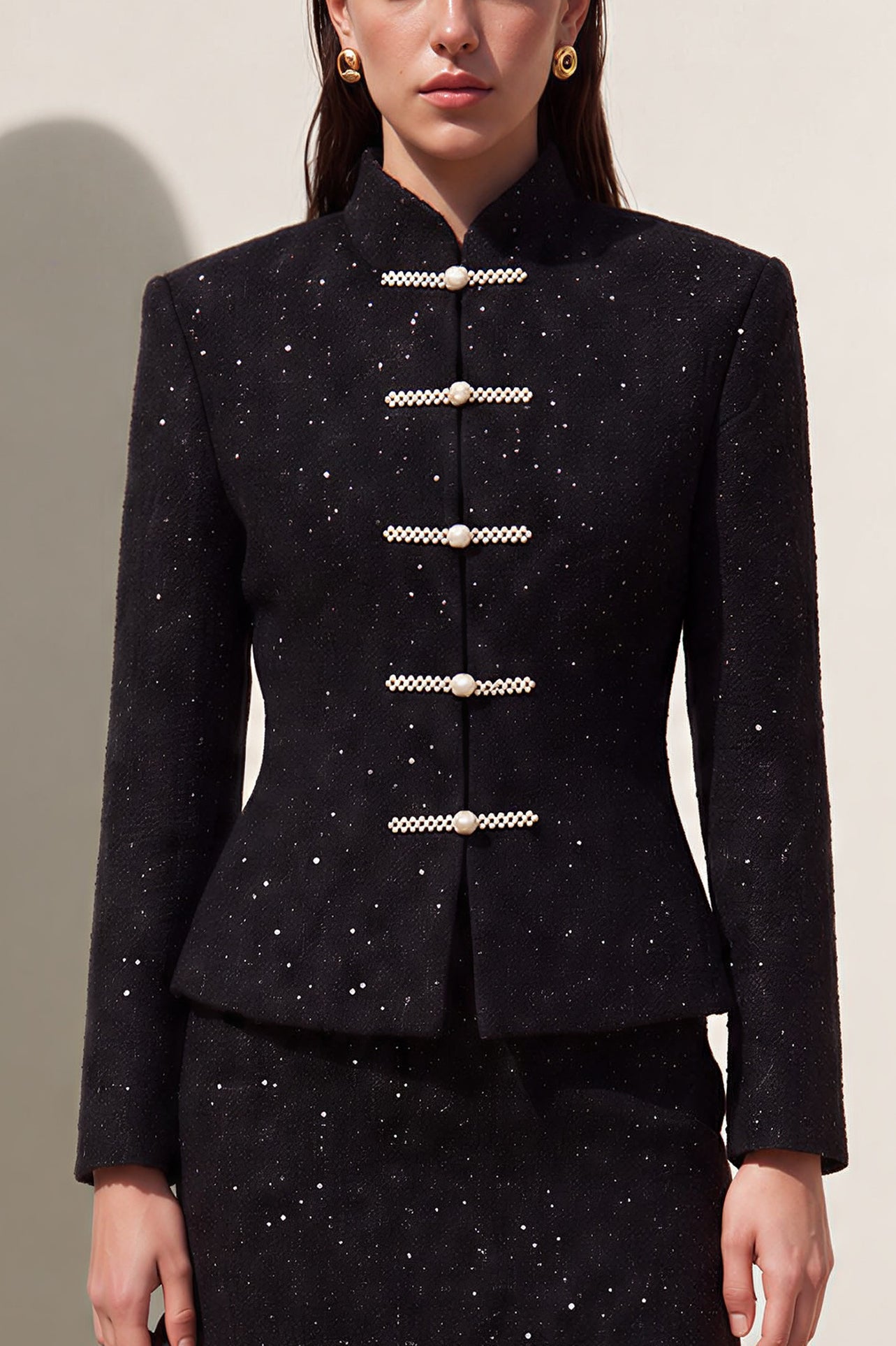 A chic woman wearing a luxurious black sparkle tweed tailored jacket featuring an authentic stand cheongsam collar, elegant horizontal pearl bar closures, and a flattering hourglass waistline.