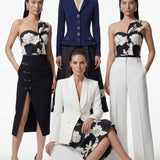 A professional woman wearing a sophisticated one-shoulder black and white floral print top, featuring a dramatic oversized bow detail on the shoulder, paired with white high-waisted trousers for an elegant evening look.